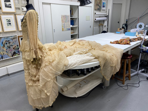 Vestido em manequim com a cauda em mesa passando sobre a etapa de conservação e restauro