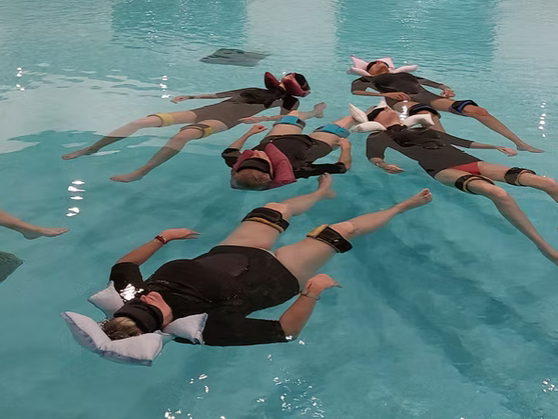 personnes qui flottent à la surface de l'eau la tête sur un coussin, flotteurs aux jambes, les yeux couverts