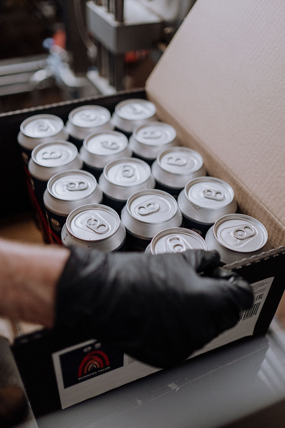 Hands packing freshly filled beverage cans for fast production turnaround.