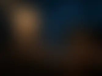 Fotografia em claro-escuro com tons de azul meia-noite profundo, focada no rosto de uma marionete de madeira iluminada sobre uma mesa escura. Seus fios desaparecem nas sombras do fundo desfocado.