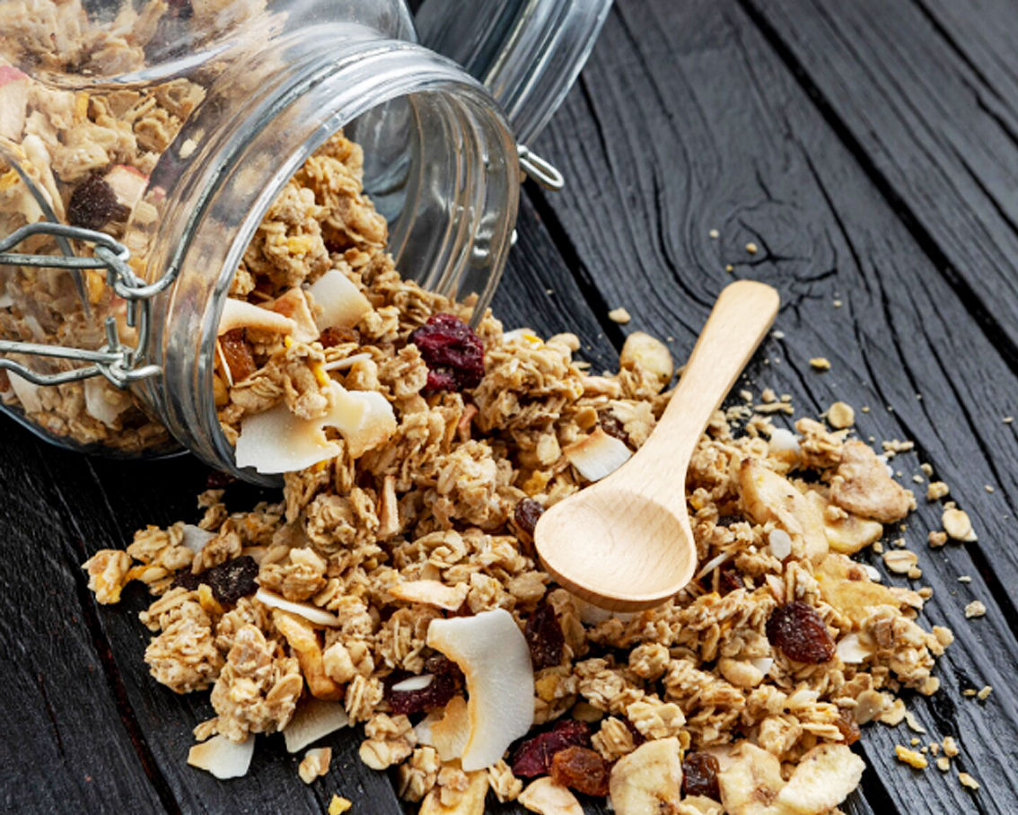 Granola που χύνεται πάνω σε μαύρο ξύλινο τραπέζι, μέσα από γυάλινο βάζο.