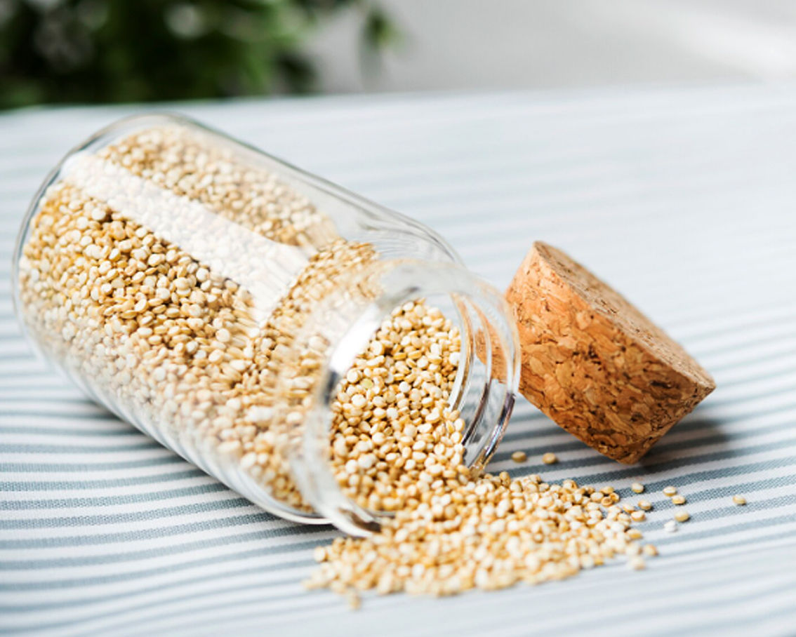 Σπόροι κινόα που χύνονται μέσα από γυάλινο βάζο σε ένα τραπέζι αφού έχει βγει ο φελλός.