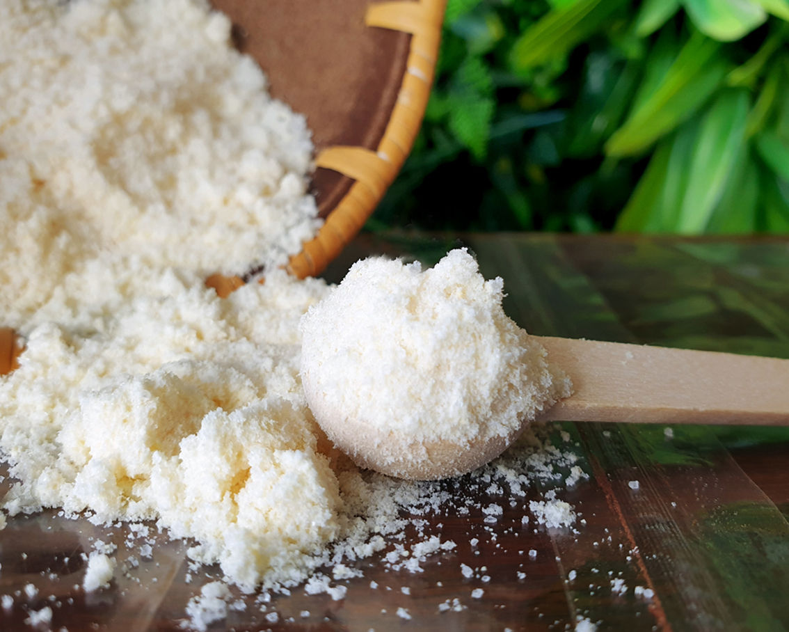 Λευκή σοκολάτα μέσα σε ξύλινο κουτάλι χυμένη επάνω σε τραπέζι και μπροτά από πρασινάδα.