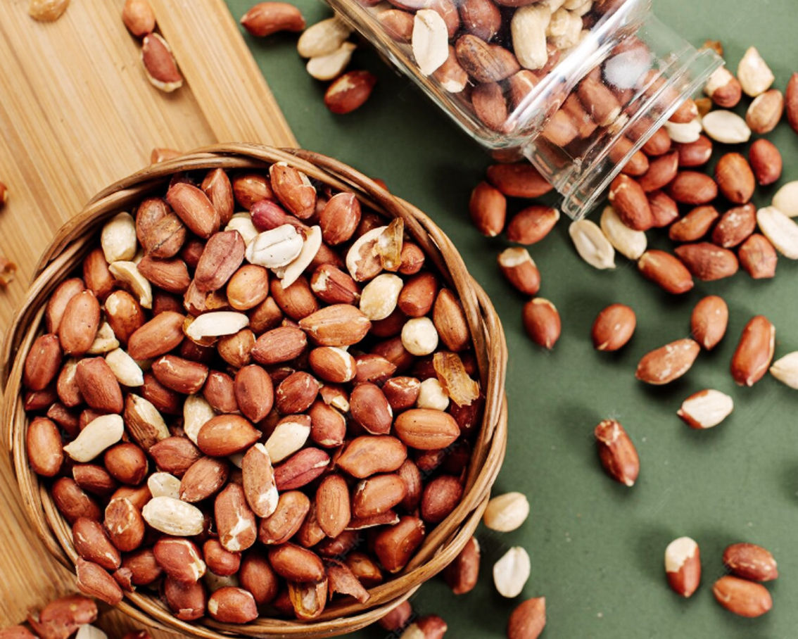 Αράπικα φυστίκια μέσα σε ψάθινο μπολ και δίπλα φυστίκια που χύνονται από ένα πεσμένο γυάλινο βάζο.