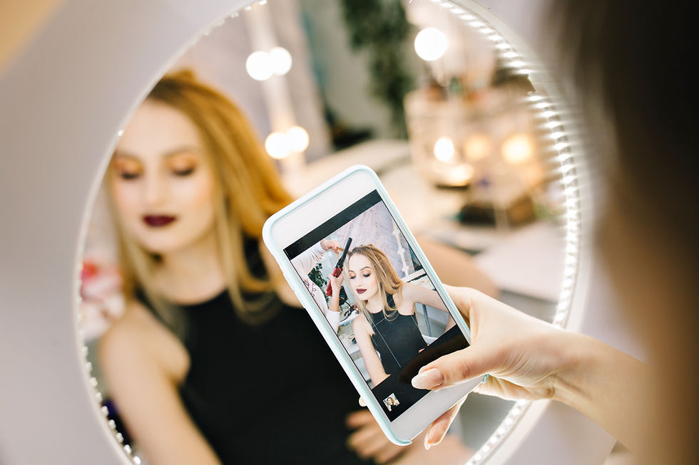 mulher jovem e maquiada em frente a um espelho segura celular que exibe uma foto sua