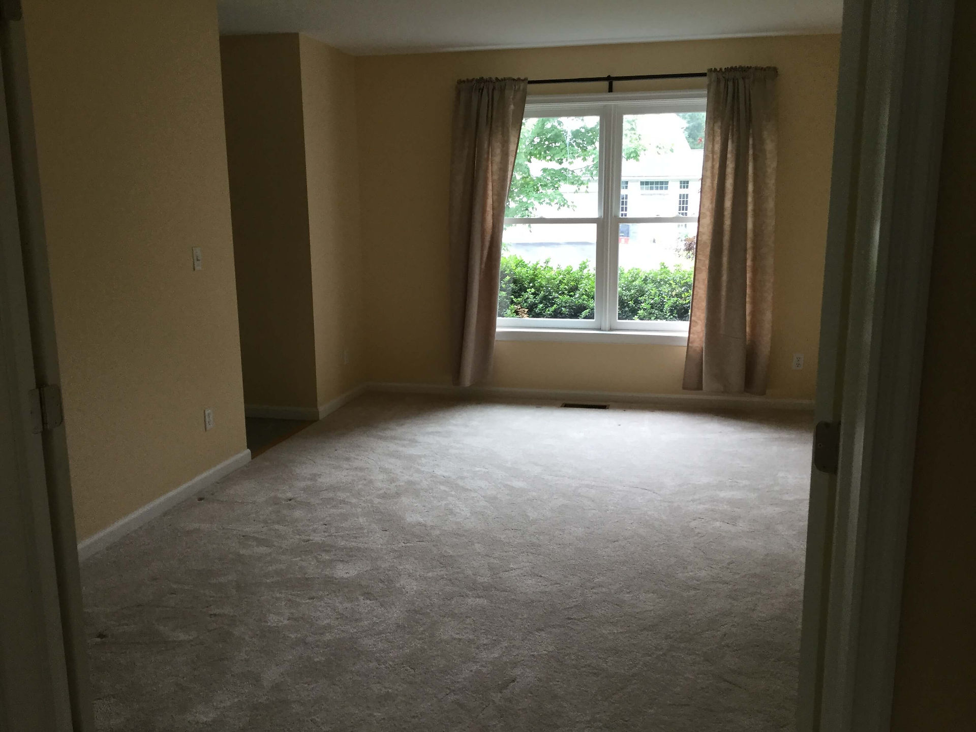 dark and empty formal living room with walls, carpet, and drapery in various shades of beige