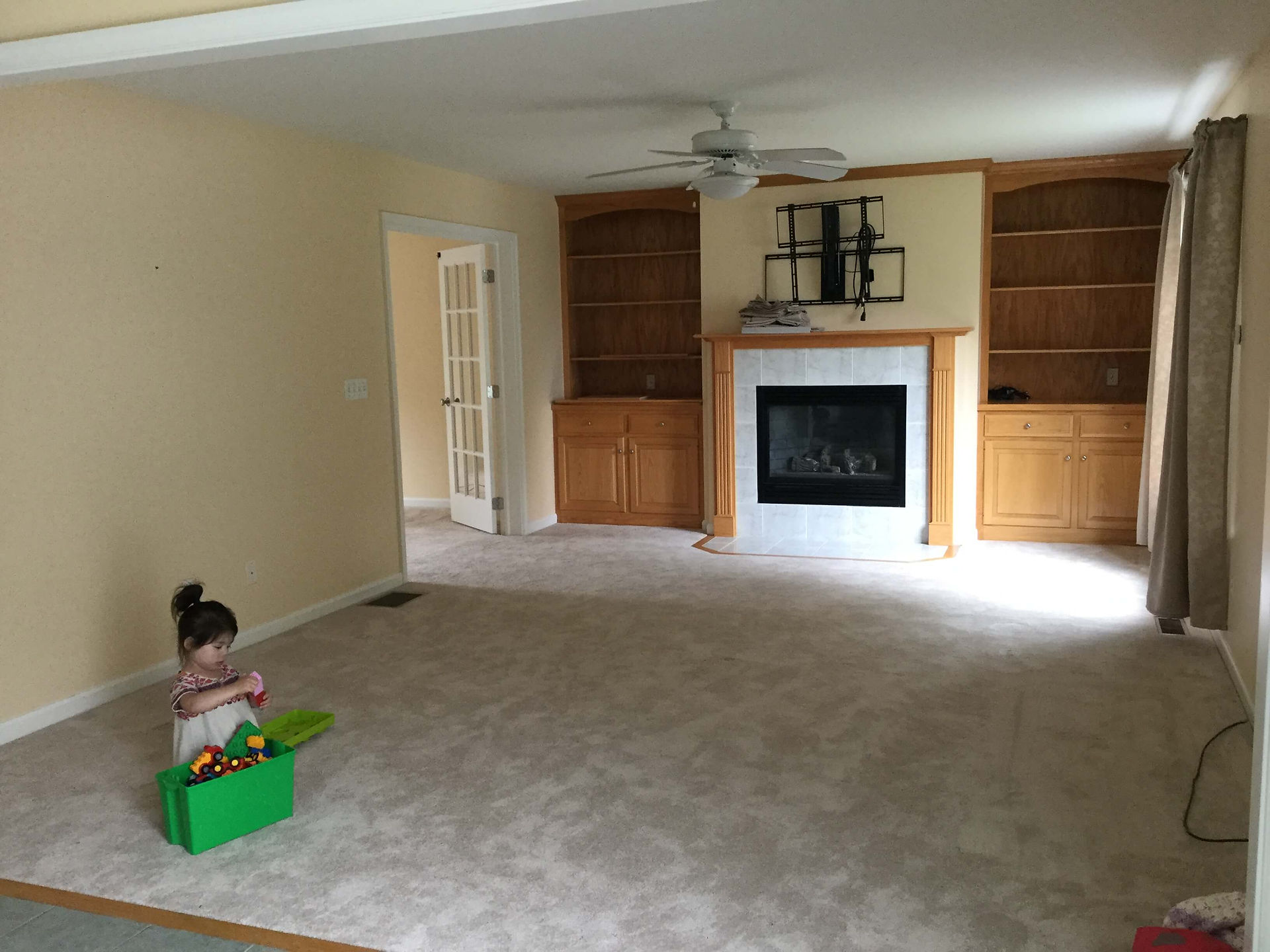 original family room with medium beige walls, honey oak built-ins, TV bracket above fireplace, and white ceiling fan light fixture