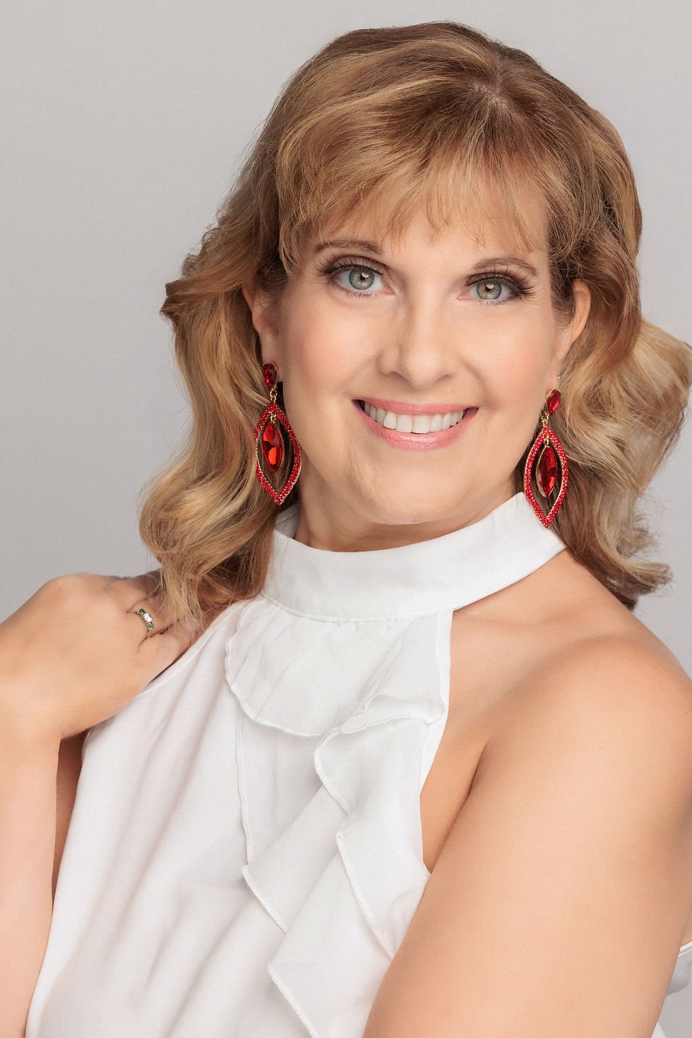 Smiling woman with blonde hair, white top, red earrings