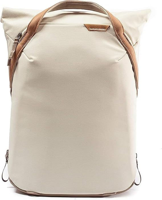 Beige canvas backpack with brown leather straps and top handle, shown front-on against a white background.