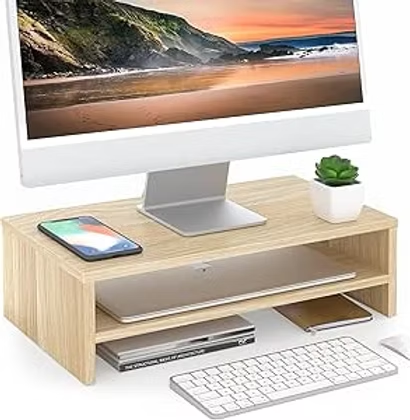 Minimalist desk setup with monitor on a wooden riser, smartphone, keyboard, laptop, and small plant on a clean white background.