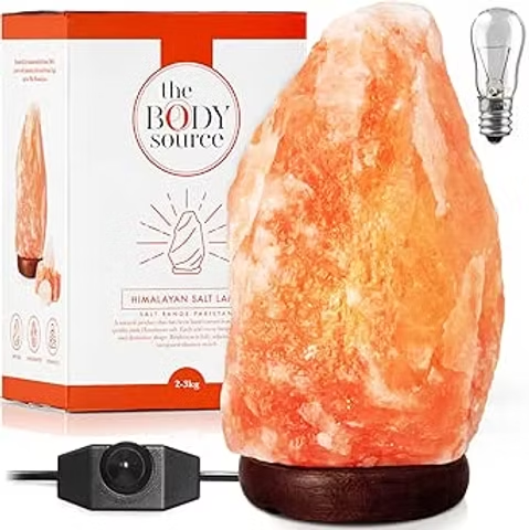 Himalayan salt lamp with orange crystal on wooden base beside box labeled The Body Source and a bulb.