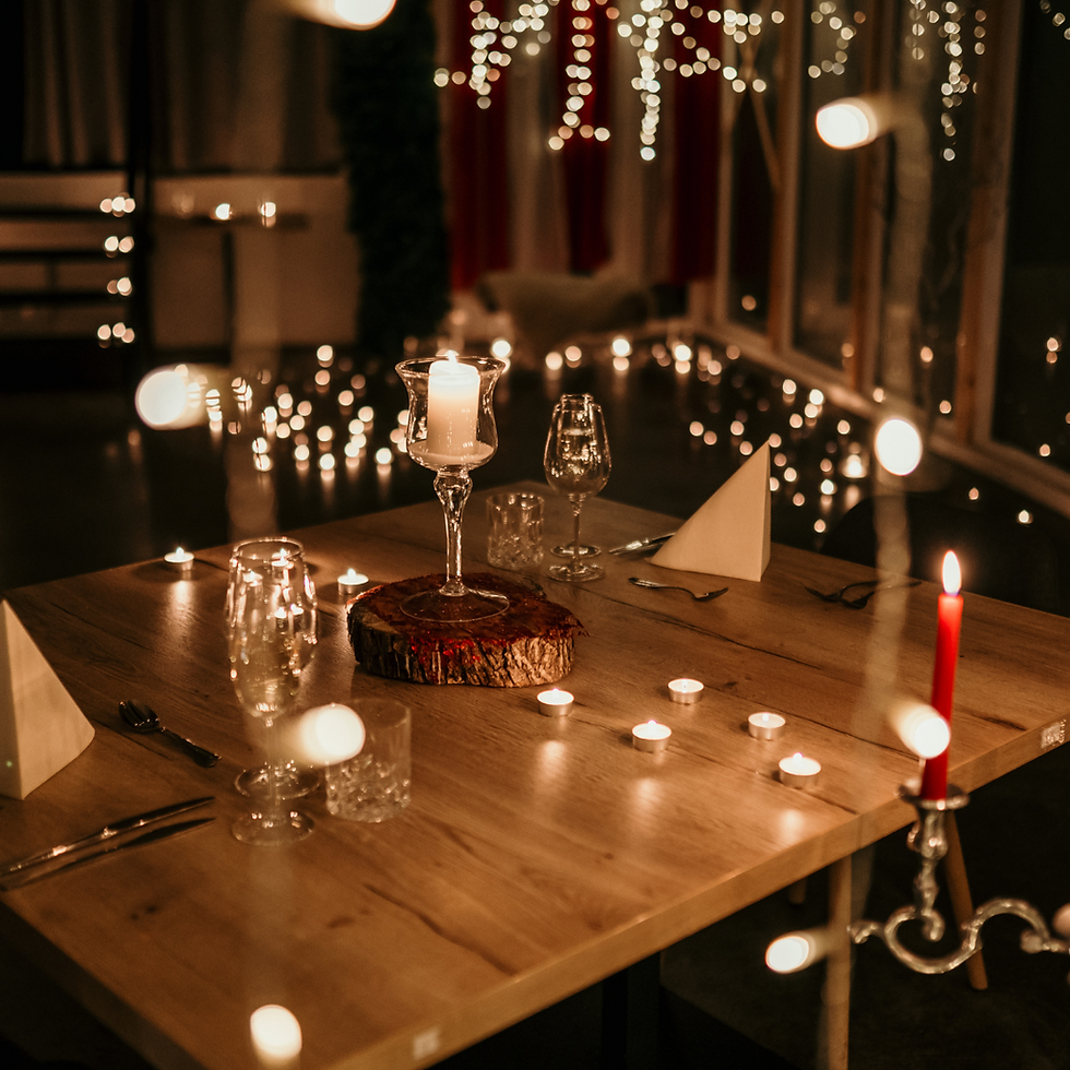 Romantic dinner setup with candles on a wooden table, wine glasses, and folded napkins. Warm lights create a cozy, intimate ambiance.
