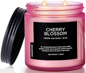 Pink candle jar labeled "Cherry Blossom, 100% Natural Wax," with a black lid beside it. Two flames lit, creating a calm ambiance.