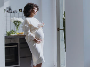 A pregnant woman looking longingly out of a window.