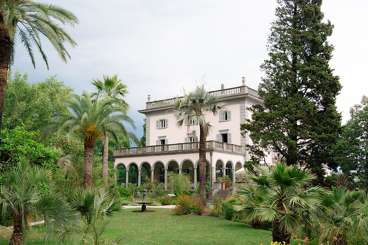 Villa Emden mit Palmen im Garten, rosa Fassade und Arkaden, eingebettet in mediterrane Parklandschaft auf der Brissago Insel am Lago Maggiore
