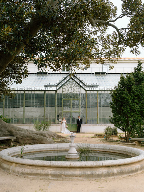 Brautpaar steht vor einem Gewächshaus im Vandelli Garten in Lissabon