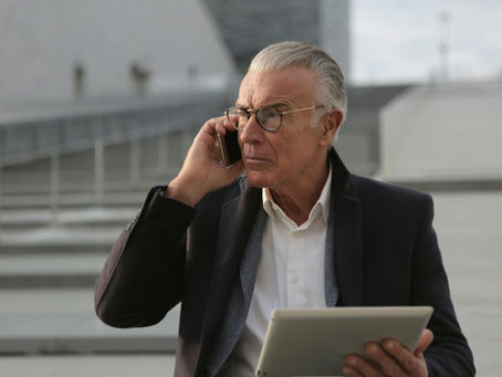 older adult man on phone holding tablet with concerned expression representing how to report a scam in Canada and contacting the Canadian Anti-Fraud Centre