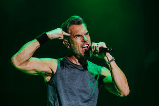 Vocalist performing with intense energy under green stage lighting, flexing with microphone in hand, photographed by Maxwell Thomason