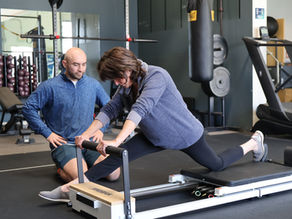 A woman with MS is using a pilates reformer while her therapist watches. 