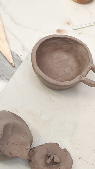 A photograph of a hand built clay mug and other bits of clay sitting on a work surface