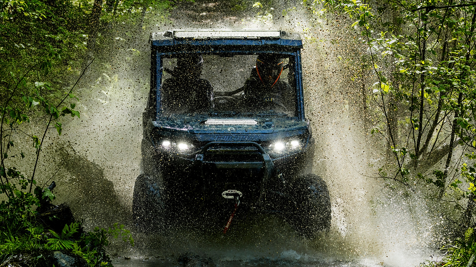 ATV splashes through a muddy forest trail, water spraying around. Dense green foliage surrounds the vehicle, adding a sense of adventure.