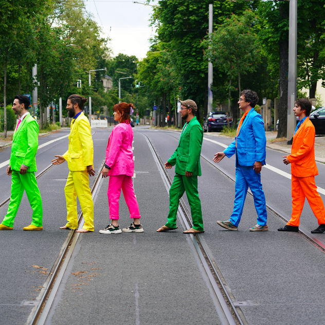 Offbeat Cooperative sechs Personen auf der Straße hintereinander in bunten Anzügen
