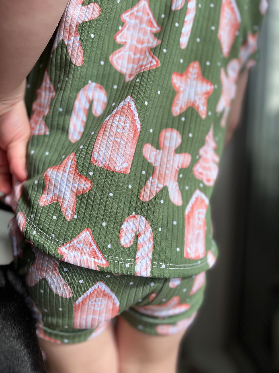 Close-up of a child in green rib knit Christmas pajamas with candy canes, stars, gingerbread houses, and people-shaped cookies.