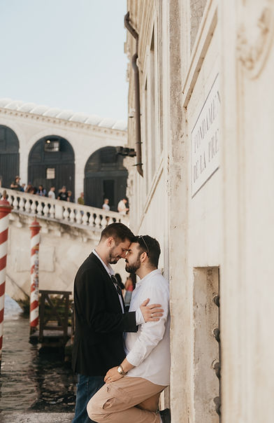 Joe and Fran standing on their profile looking into each other, close to kissing, in front of Rialto's bridge in Venice