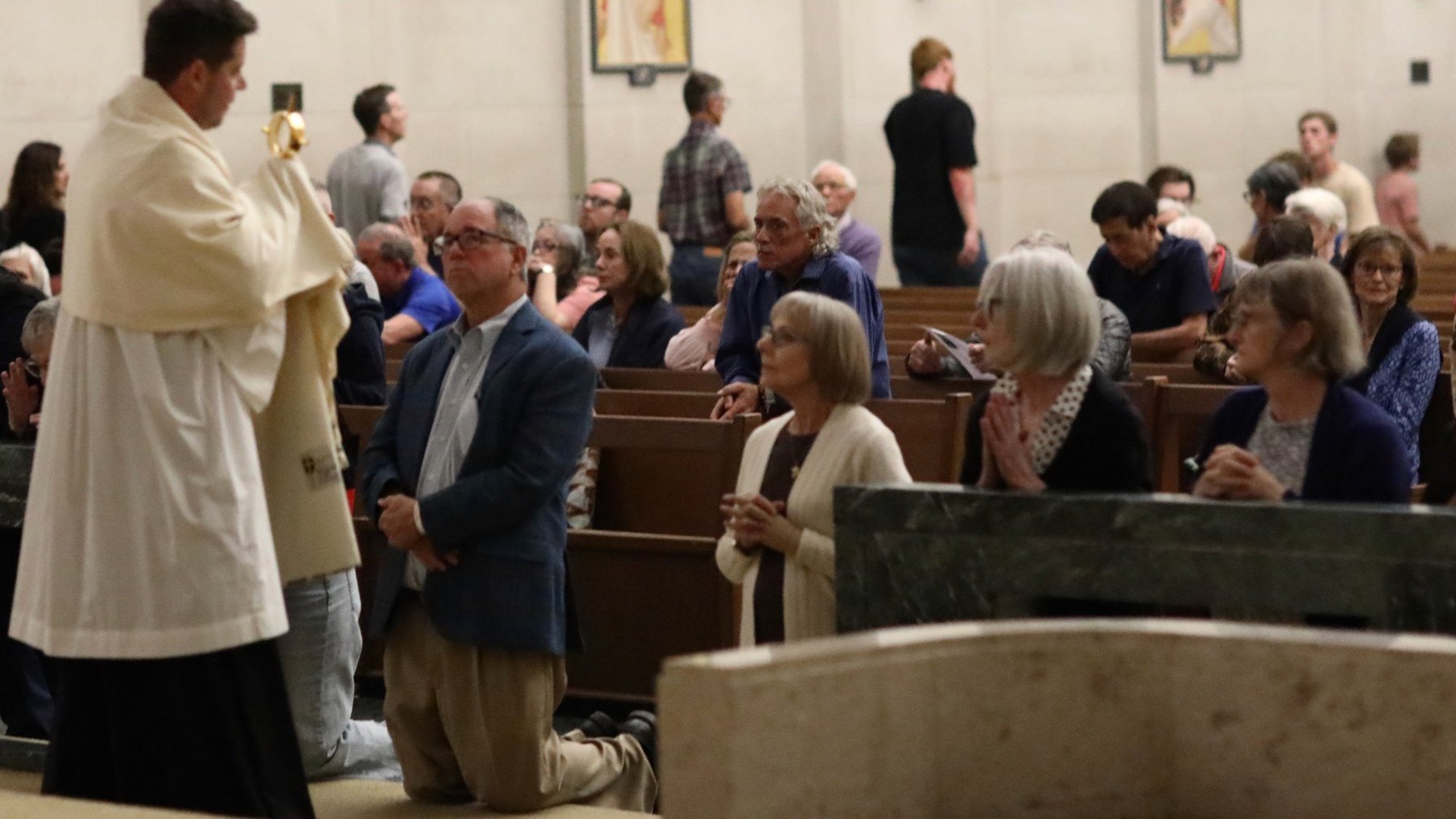 A priest carries the Eucharist past kneeling parishioners