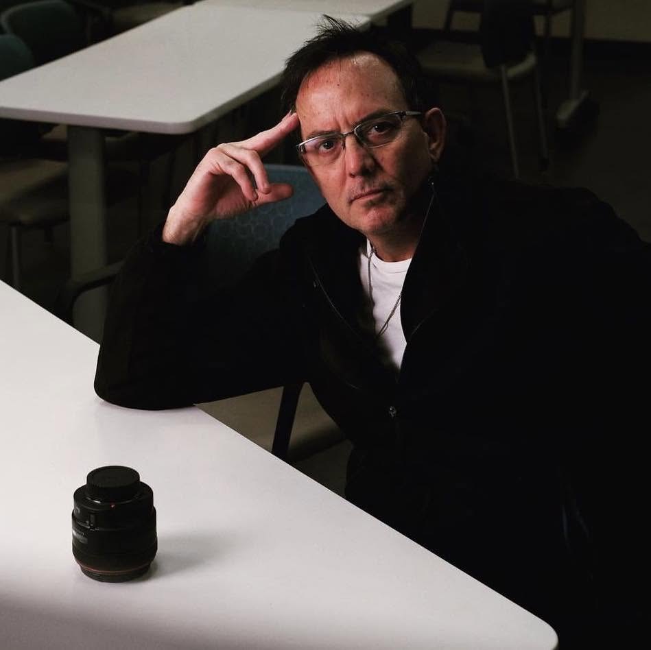 Dan Renaud seated at a table beside a camera lens