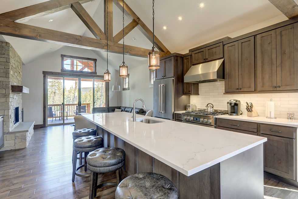 Spacious kitchen with wooden beams, stone fireplace, large island, and stainless appliances. Bright with natural light from large windows.