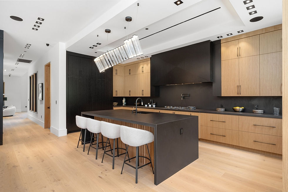 Modern kitchen with light wood cabinets, black countertops, and a large island with gray barstools. Pendant lights hang above on a wood floor.