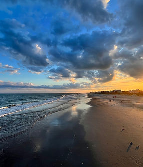 Sunset At Surfside Beach Featuring A Long Pier, Ocean Waves, Golden Reflections On Wet Sand, And A Dramatic Cloud-Filled Sky