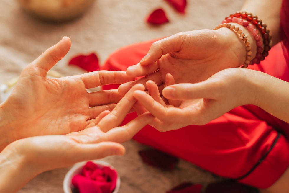 Two hands performing a gentle hand massage. Red petals and fabric in the background create a calm, soothing atmosphere.