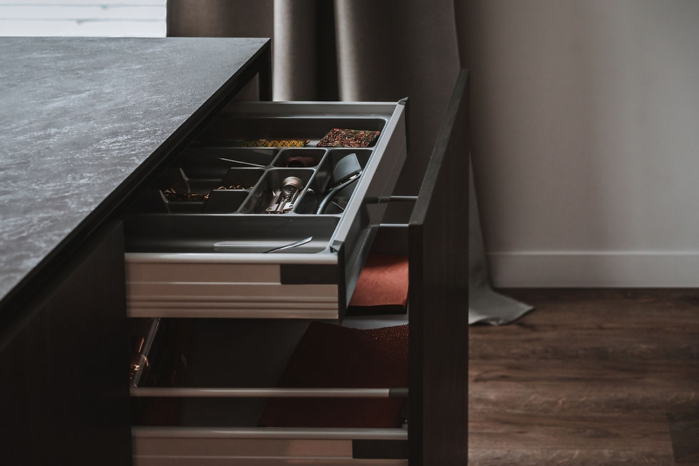 Open kitchen drawer with cutlery and utensils, set in a modern kitchen with dark wood flooring and grey curtains in the background.