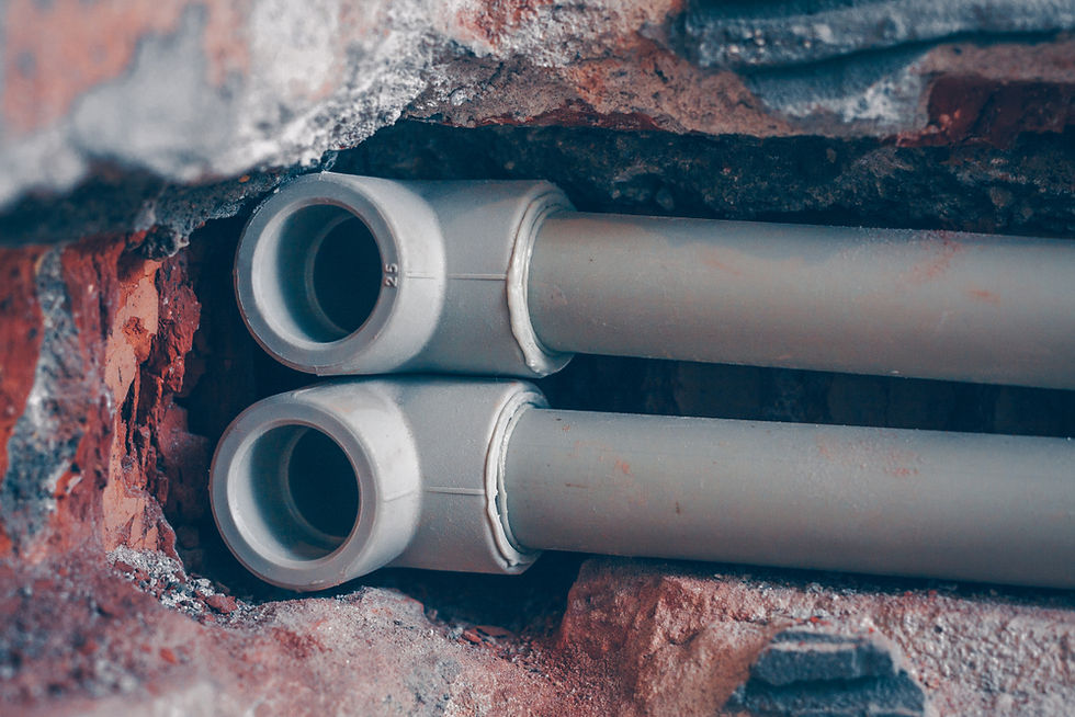 Two gray PVC pipes embedded in a brick wall. The rough textures of the bricks contrast with the smooth pipes, creating an industrial feel.