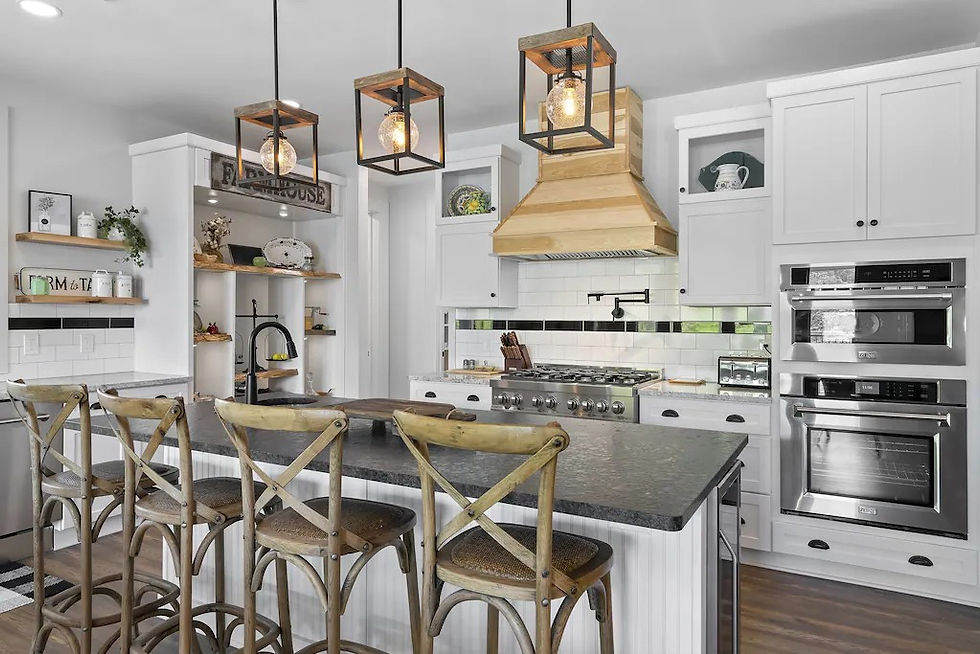 Bright farmhouse kitchen with island and four stools, white cabinets, wood hood, pendant lights, and stainless steel double ovens.