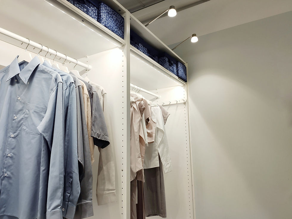 Shirts in shades of blue and beige hang neatly in a white closet with overhead lights and blue storage boxes, creating an organized look.
