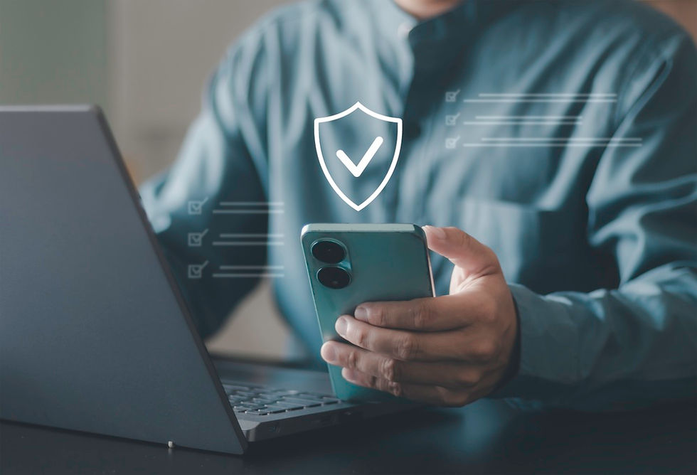 Person in teal shirt holds a smartphone, checking it while using a laptop. A digital shield with a checkmark hovers, symbolizing security.