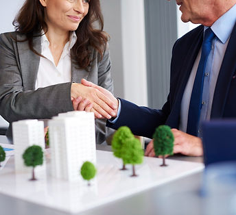 two professionals shaking hands over a miniature real estate model