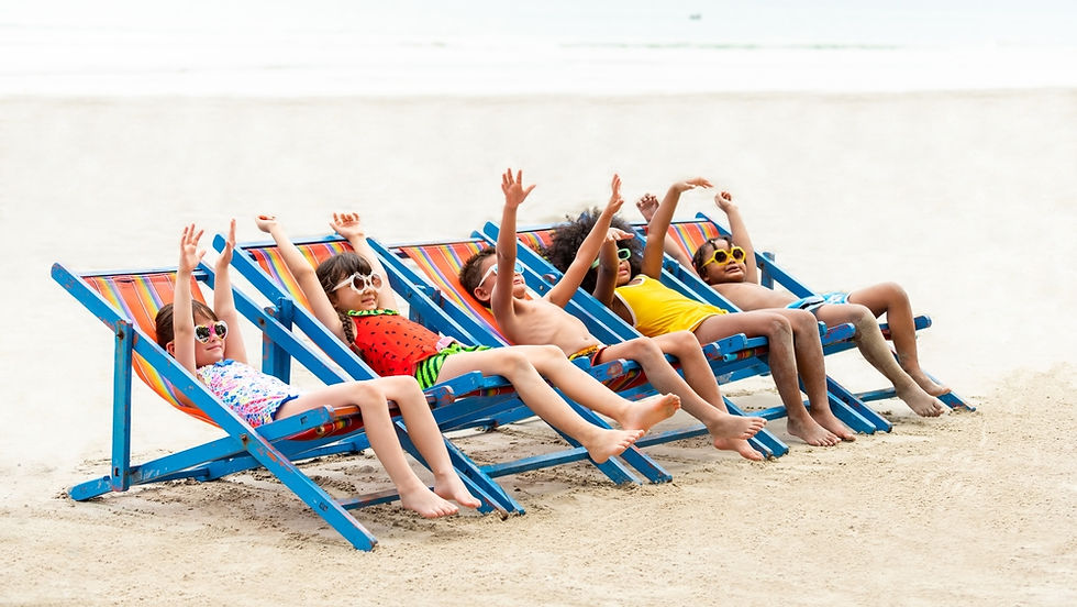 Five kids in swimsuits and sunglasses lounge joyfully on bright beach chairs, arms raised, on a sandy beach with a calm sea backdrop.