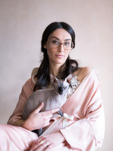 Portrait de face d’une femme sensuelle en kimono rose poudré, avec son sphynx sur les genoux, tous deux le regard fixe vers l’objectif.