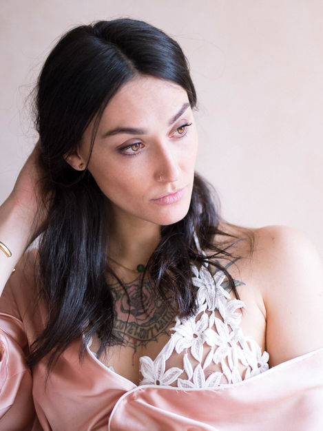 Portrait pur et intime d’une femme brune songeuse, vêtue d’une chemise de nuit rose poudré.