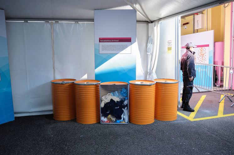 Fünf orange Abfallfässer in einem Zelt, eines davon mit sichtbarem Inhalt; daneben eine Infotafel zur Abfallklassifizierung am Tag der offenen Tür des ZWILAG.