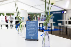 Festlich dekorierter Stehtisch mit Blumen und Informationskarte im Zelt des Jubiläumsfests.