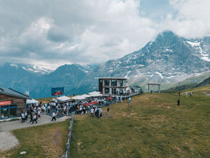 Berglandschaft in Grindelwald mit verschneiten Alpen im Hintergrund und einer gut besuchten Event- und Gastronomiefläche der Schindler X8 auf einer grünen Bergwiese.