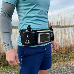 Loper draagt zwarte Hen Sportsgear heuptas met flessen en telefoon, buiten.
