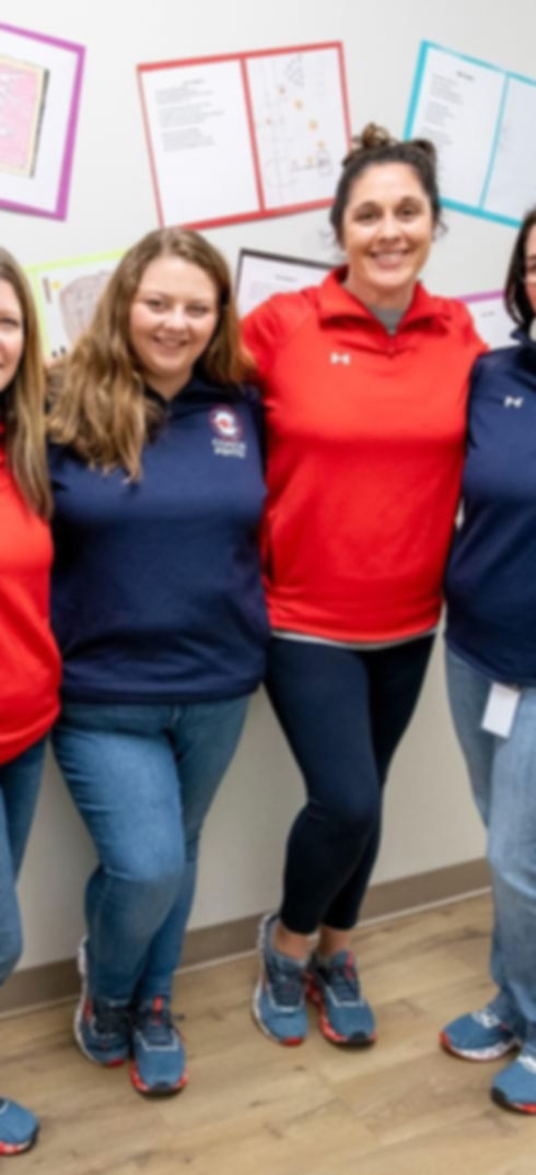 Four women teachers, standing together in the hallway smiling.