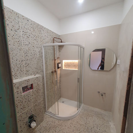 Moderní koupelna se sprchovým koutem, obklady a kulatým zrcadlem.