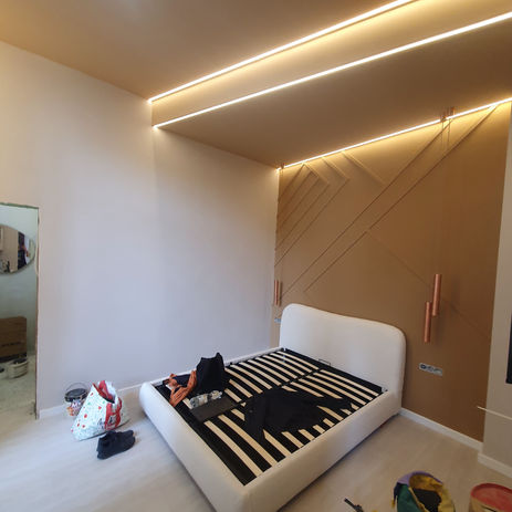 Interiér moderní ložnice s postelovým rámem, dřevěným panelem a LED osvětlením.